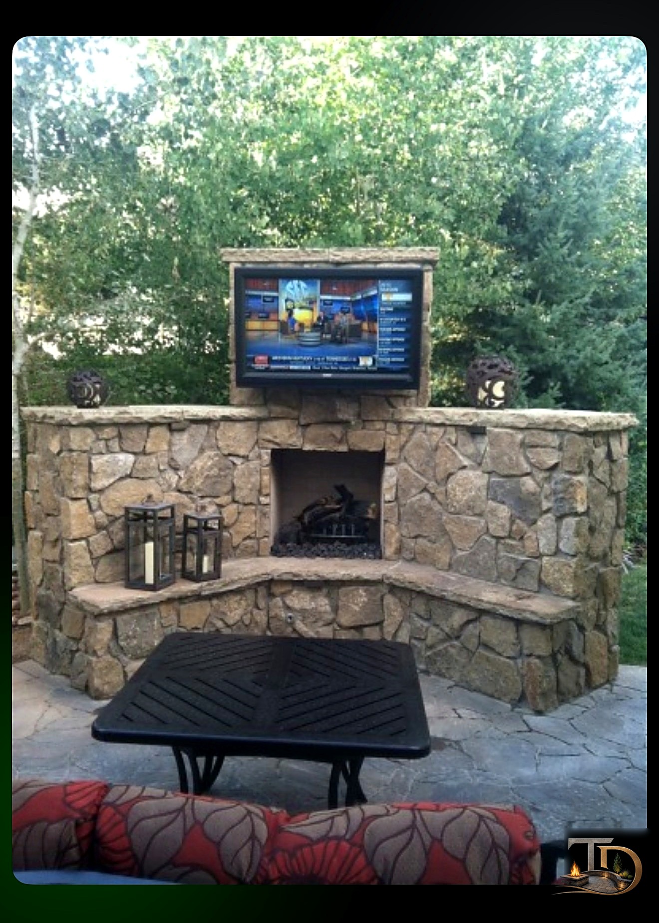 Stone outdoor fireplace with mounted television beneath a covered patio