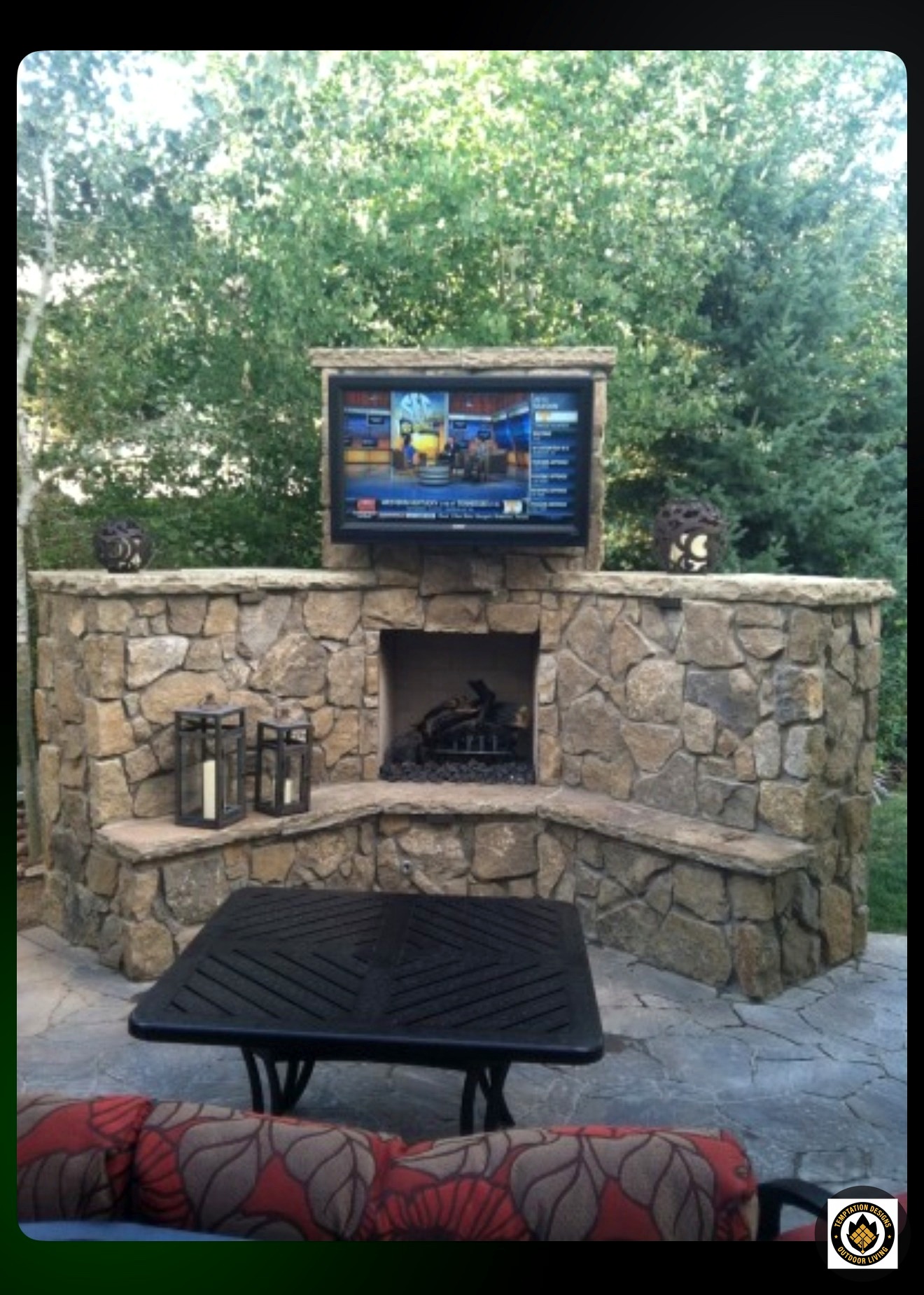 Stone outdoor fireplace with mounted television beneath a covered patio